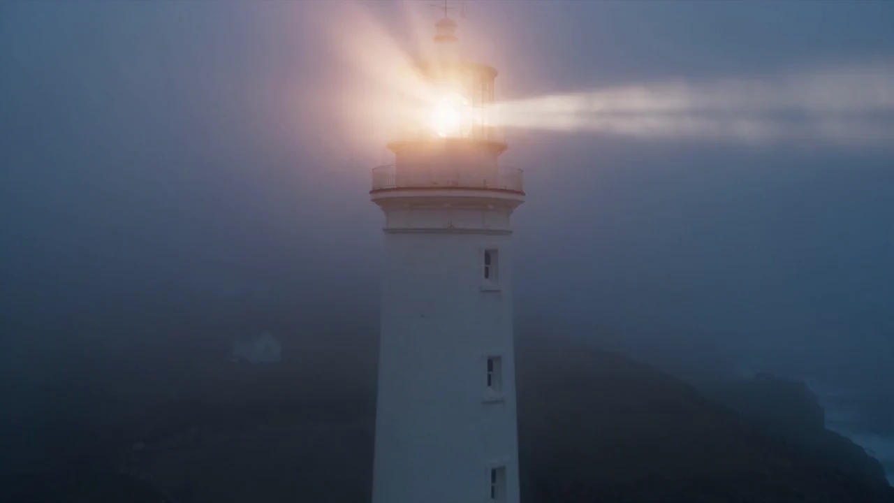 A lighthouse beam sweeping a stormy sea at dusk