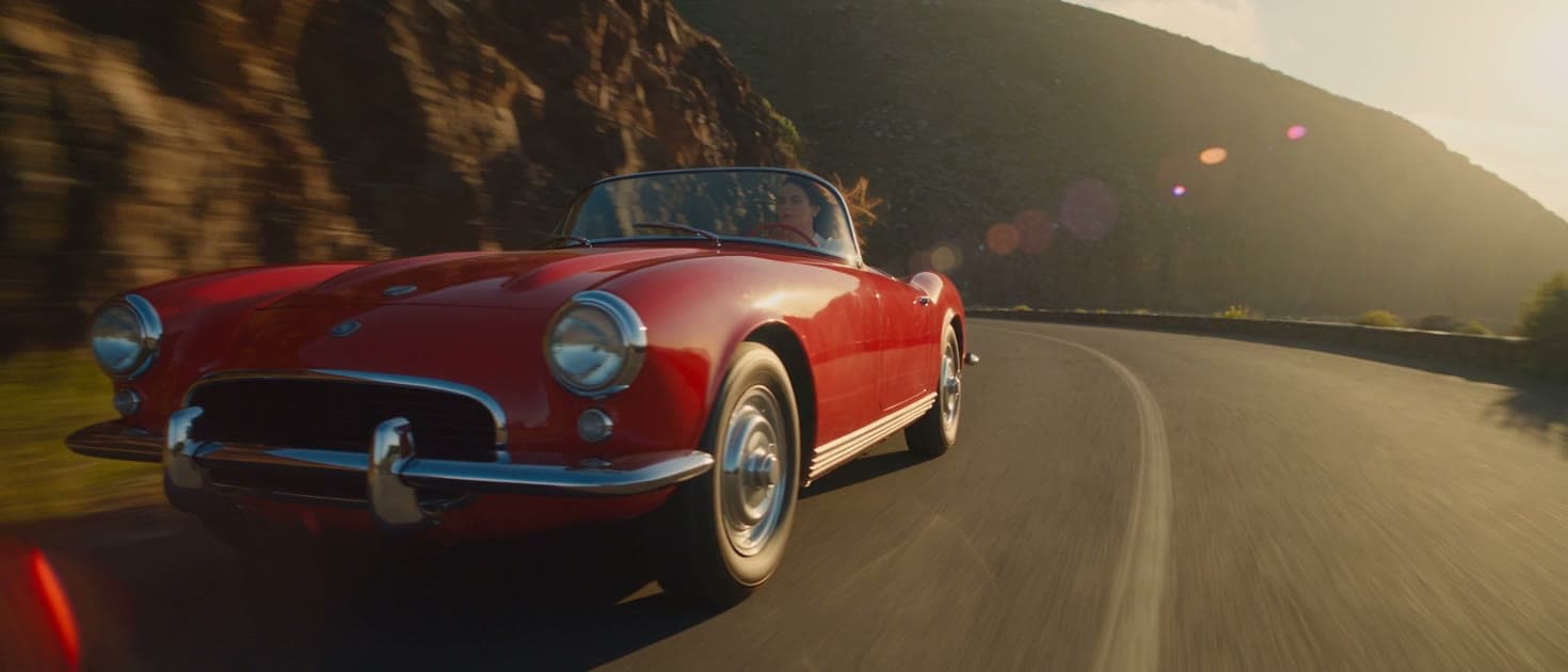 A red vintage convertible on a coastal mountain road at golden hour, framed in 21:9 and rendered on the Premium engine